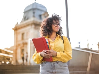 new college student In Yellow Jacket Holding Books in front university building. should her parents get power of attorney?