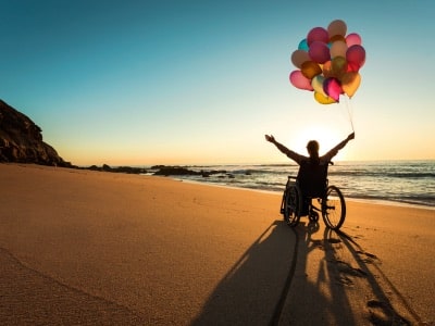 person with special needs trust in wheelchair holding balloons on beach